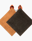 Two suede pot holders, one Tan and one Black, both with a Terracotta hanging strap, on a white background.