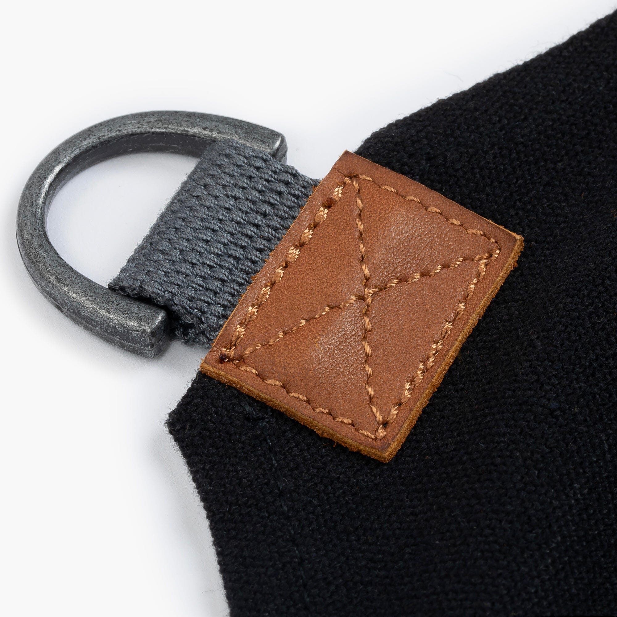 Close-up of a black strap with a brown leather tag and metal ring on a black apron with a with a white background.