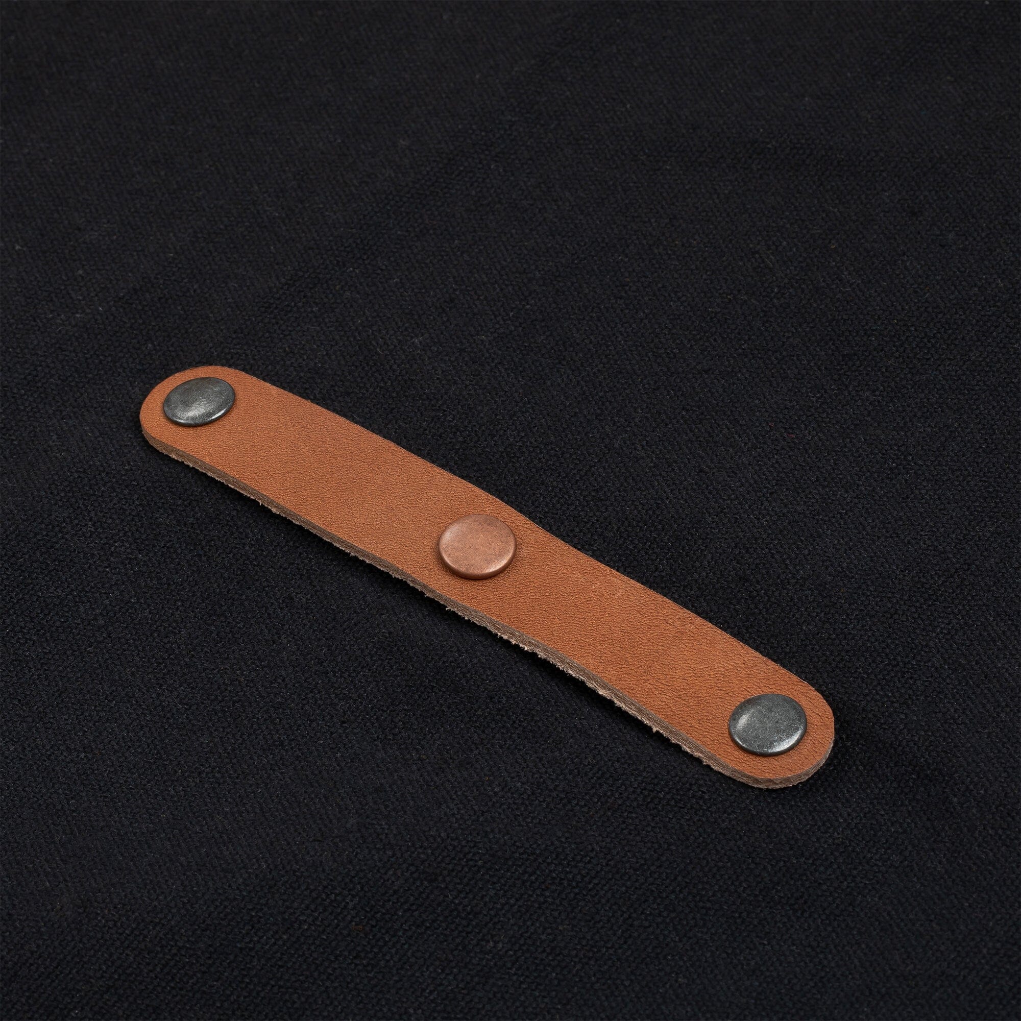Close-up of a brown leather strap with metal studs on the front of a black apron.