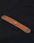 Close-up of a brown leather strap with metal studs on the front of a black apron.
