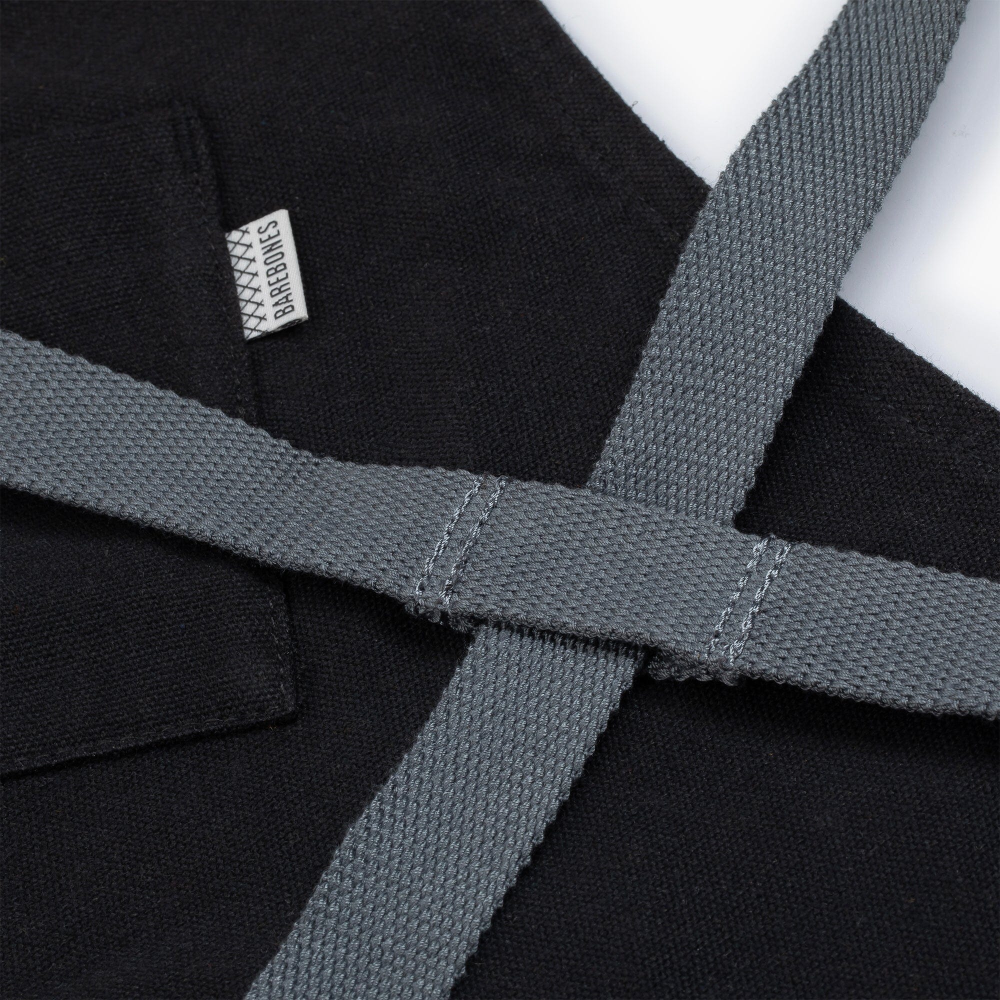 Close-up of a black apron with gray straps and visible Barebones brand label.